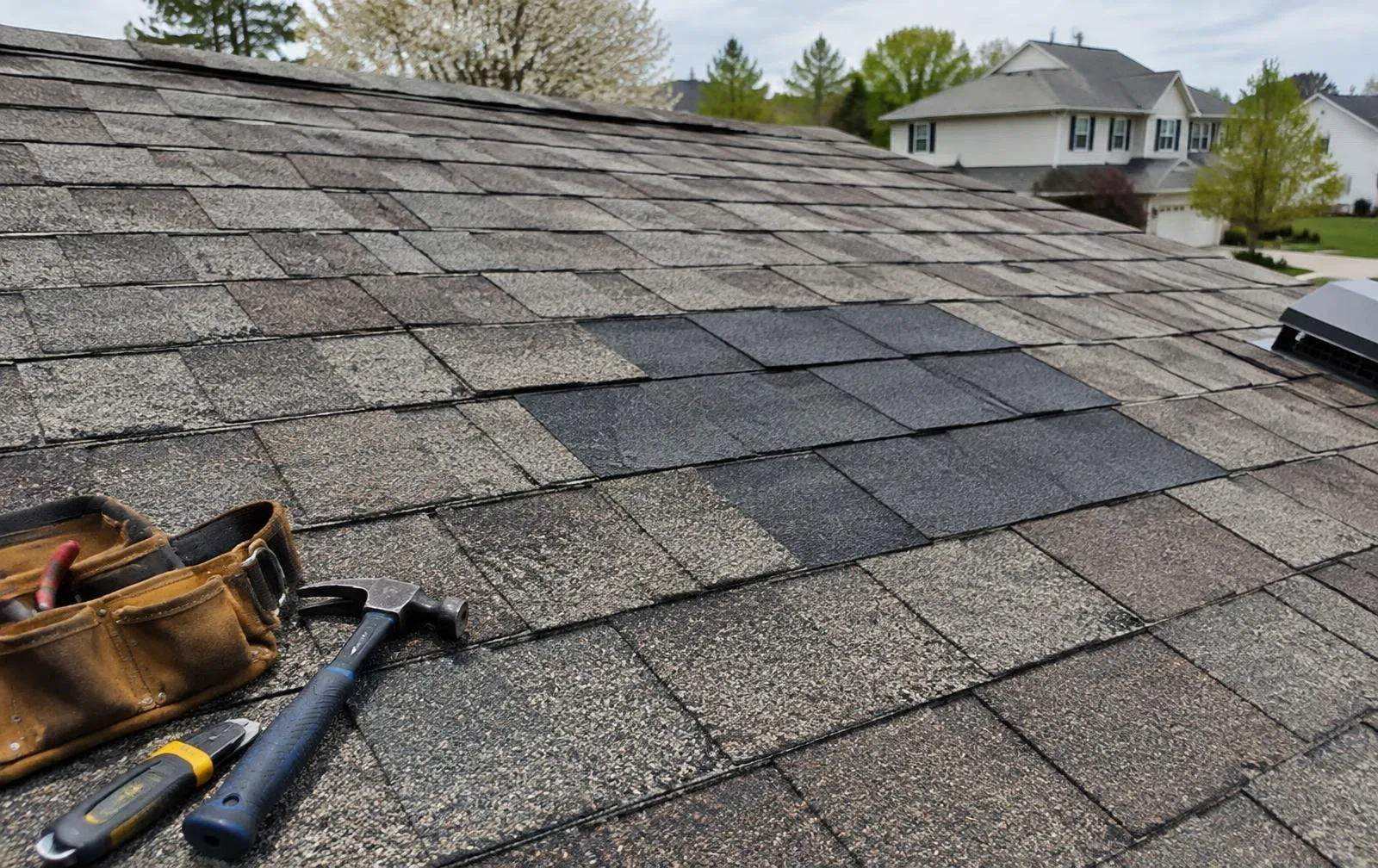 Asphalt shingle roof with freshly patched replacement shingles and tools on a New Jersey home